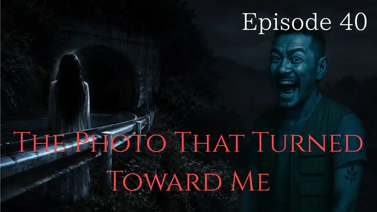 A ghostly woman standing near a dark mountain tunnel while slowly turning toward the viewer from beyond the guardrail.